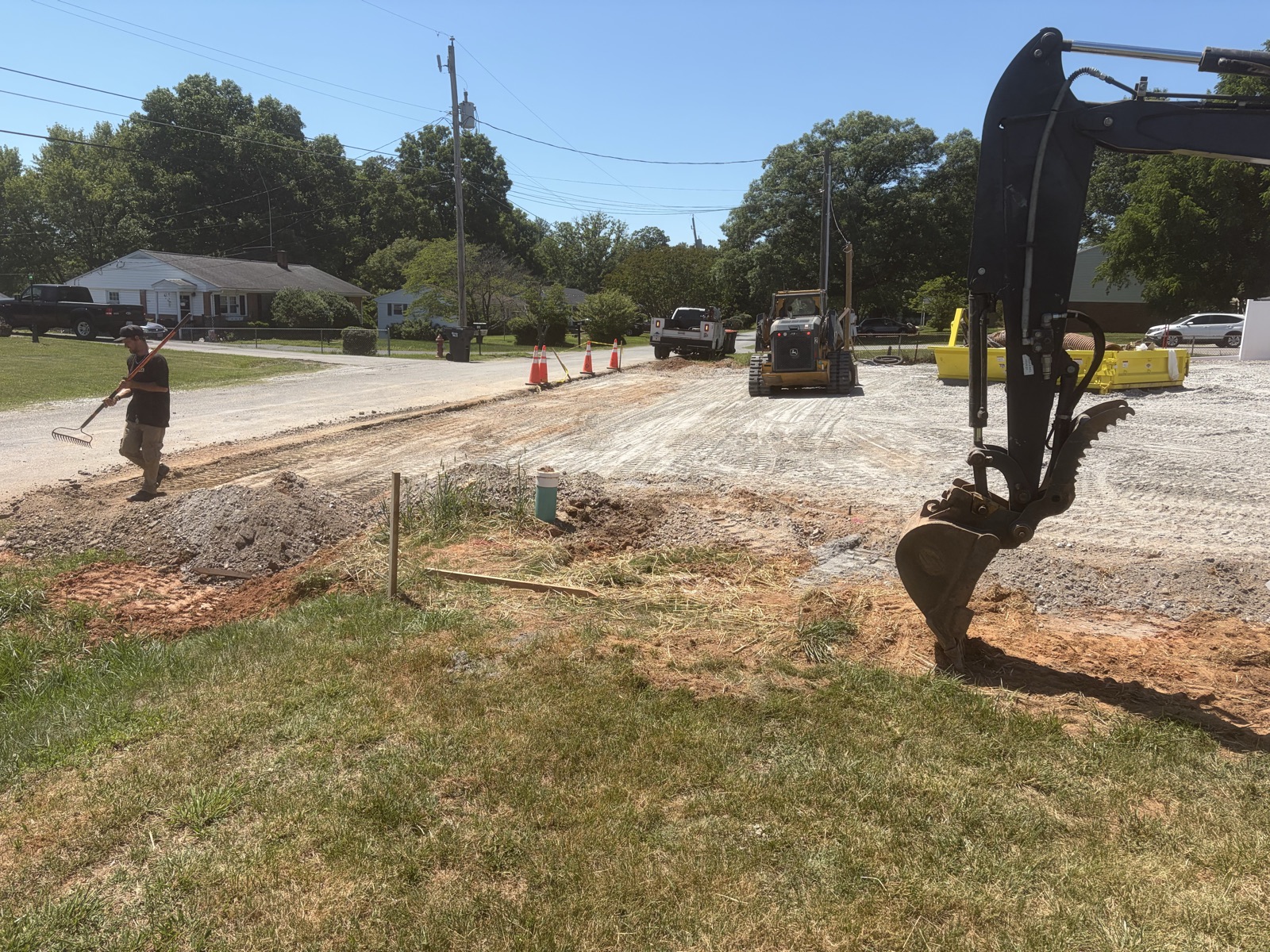 Underground drain line trenching along a residential street with excavator staged on site