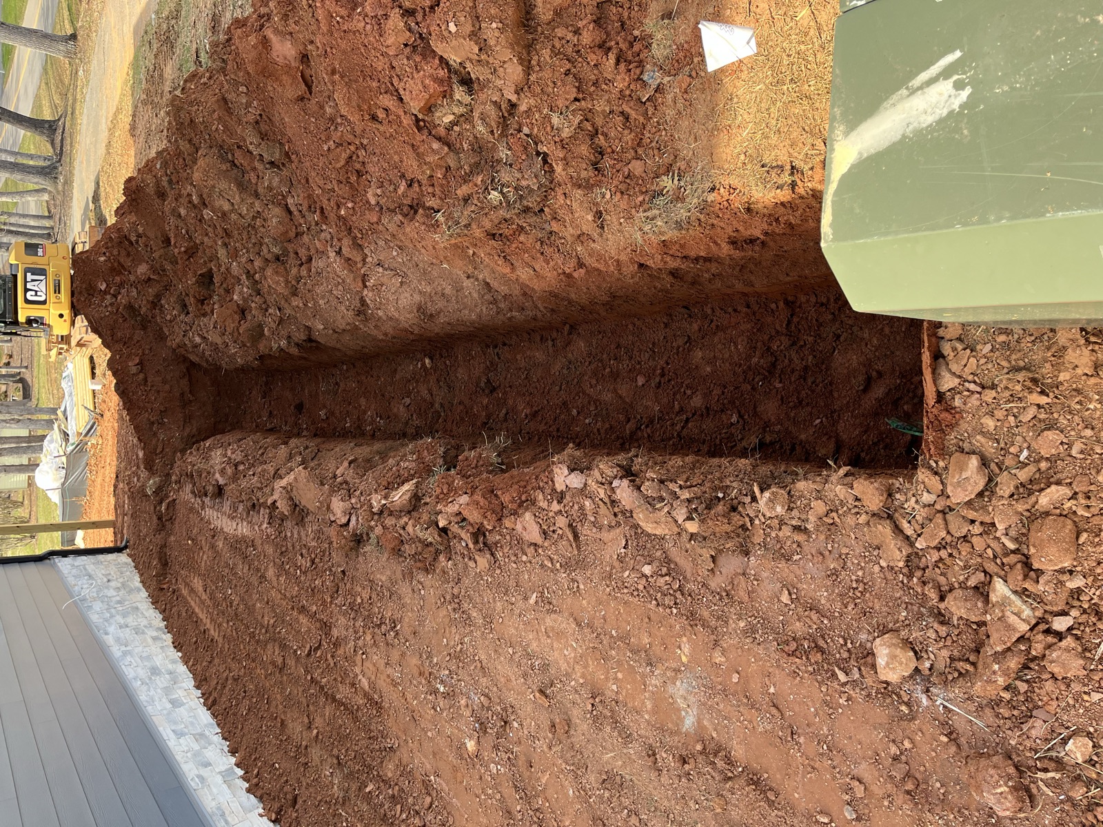 Deep utility trench excavated alongside a house foundation