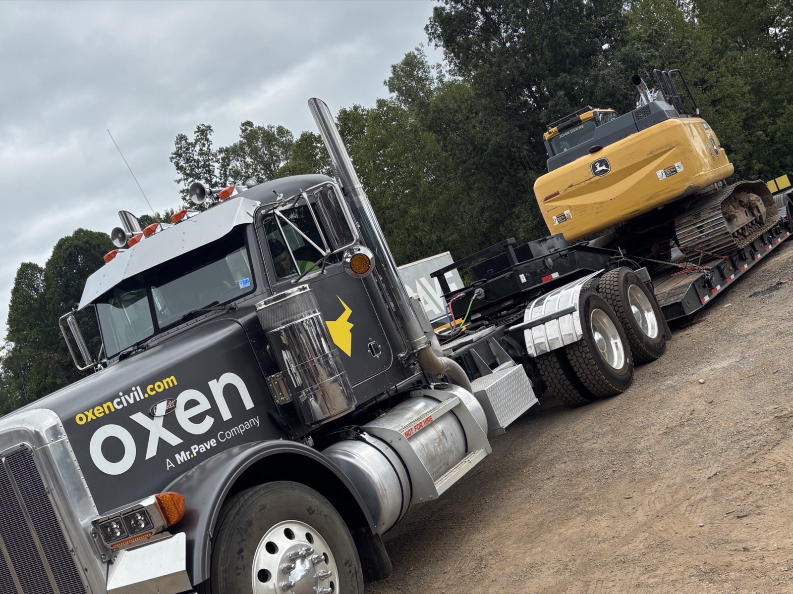 Oxen Civil truck and lowboy trailer hauling a tracked excavator off an active jobsite